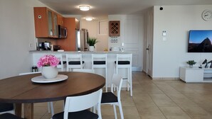 Une cuisine moderne avec des meubles blancs, une table à manger avec des chaises et un téléviseur fixé au mur.