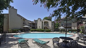 A pool area with lounge chairs and umbrellas, surrounded by apartment buildings. - CITY CONDO (Houston)