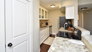 A modern kitchen with white cabinetry, a black stove, and a granite countertop. - CITY CONDO (Houston)