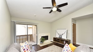 A living room with a fireplace, a ceiling fan, and a sliding glass door leading to a balcony. - CITY CONDO (Houston)