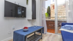 A modern living room with a flat-screen TV, a small table with a bowl of fruit, a bench, and a blue sofa. - Beautiful apartment for 4 guests with pool, A/C, WIFI, TV and balcony (Lloret De Mar)