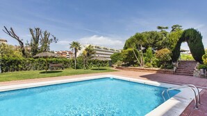 A rectangular swimming pool with clear blue water, surrounded by a brick patio, palm trees, and a well-maintained lawn. - Beautiful apartment for 4 guests with pool, A/C, WIFI, TV and balcony (Lloret De Mar)