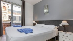 A modern hotel room with a large bed, two bedside lamps, a small bedside table, and a view of a brick building through a sliding glass door. - Beautiful apartment for 4 guests with pool, A/C, WIFI, TV and balcony (Lloret De Mar)
