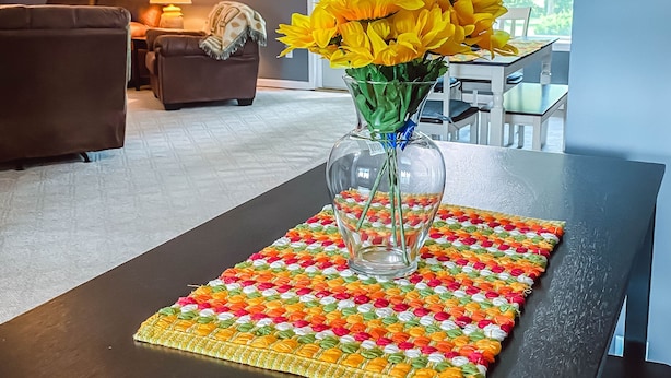 Een woonkamer met een donkerbruine salontafel, een vaas met gele bloemen en een kleurrijke geweven onderzetter.