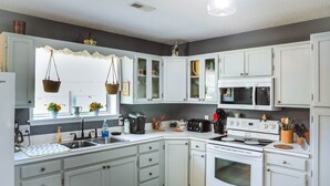 Een moderne keuken met witte kastjes, een magnetron, een fornuis en diverse keukenapparaten.