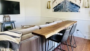 Una sala de estar moderna con una mesa de comedor de madera, sofás grises y un televisor de pantalla plana montado en la pared.