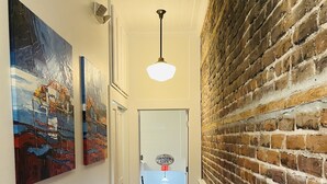 Un pasillo con piso de madera, pared de ladrillo y una puerta señalizada con 