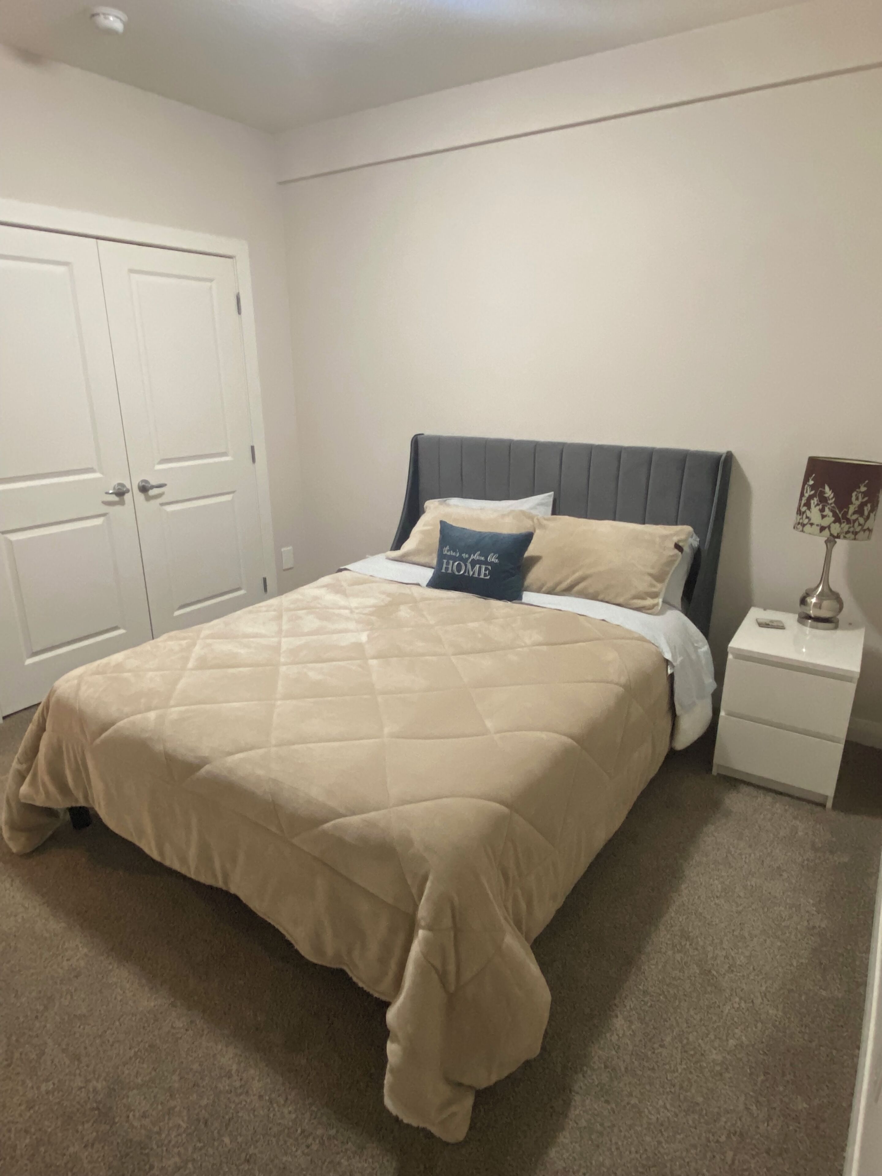 Un dormitorio con cama, mesita de noche, lámpara y puerta.