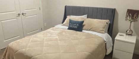 Un dormitorio con cama, mesita de noche, lámpara y puerta.