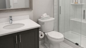 Et moderne badeværelse med en hvid vask, mørke skabe, toilet og en brusekabine i glas.