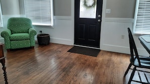Una habitación con una puerta negra, un sillón verde y una mesa de comedor con sillas.