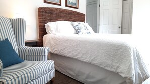 Un dormitorio con una cama grande, un sillón a rayas y dos cuadros en la pared.
