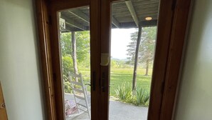 A wooden door with a glass panel, leading to an outdoor area with a bench and a view of greenery.