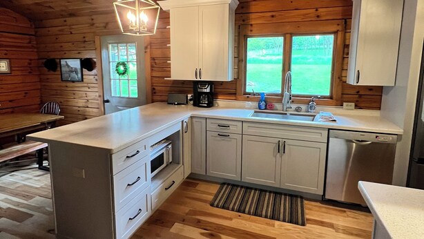 A kitchen with wooden walls and ceiling, white cabinets, a central island, and a window with a view of greenery.