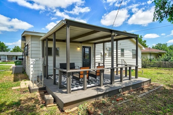 Eenlaags huis met een overdekte veranda, een voordeur en een klein zitgedeelte buiten met twee stoelen.