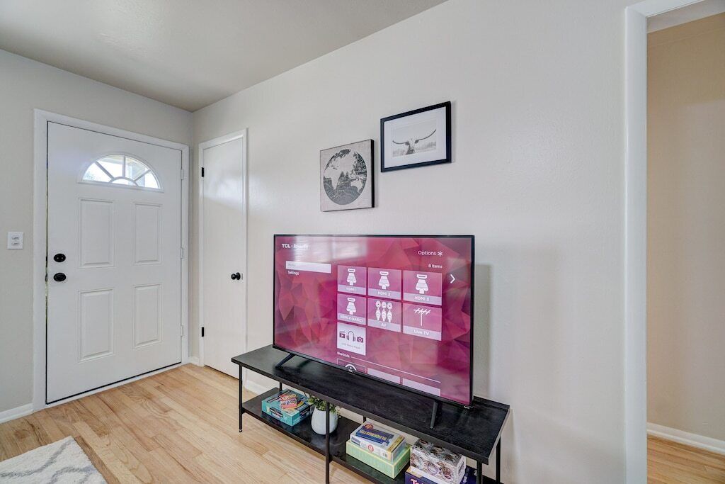 A living room with a flat-screen TV on a black stand, a white door, and two framed pictures on the wall.