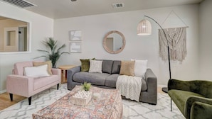 Ein Wohnzimmer mit grauem Sofa, einem rosafarbenen Sessel, einem grünen Sessel, einem Couchtisch und einer Stehlampe.