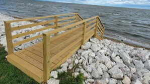 Une jetée en bois, dotée d’une rambarde, s’étend jusqu’à une côte rocheuse bordant une étendue d’eau.