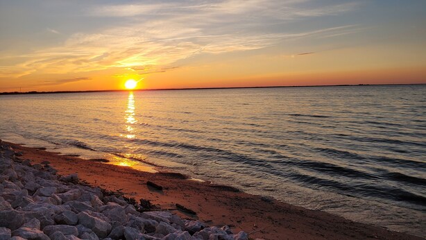Un coucher de soleil sur une mer calme, avec une côte rocheuse.