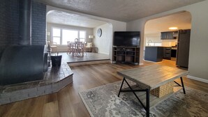 Un vaste espace de vie comprenant un coin salon avec cheminée, une table à manger et une cuisine en arrière-plan.