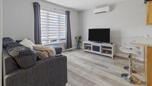 A modern living room with a grey sofa, a flat-screen TV, a white coffee table, and a wooden dining table with bar stools. - *WOW!!* Executive cozy home with 3 beds, work station & gym (St. John's)