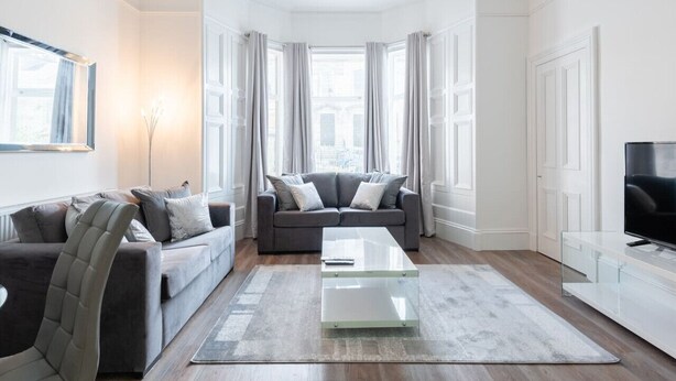 Een moderne woonkamer met een grijze bank, een glazen salontafel en een televisie op een wit kastje.
