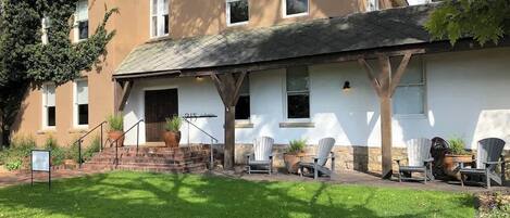 A two-story building with a covered porch, outdoor seating, and a well-maintained lawn.