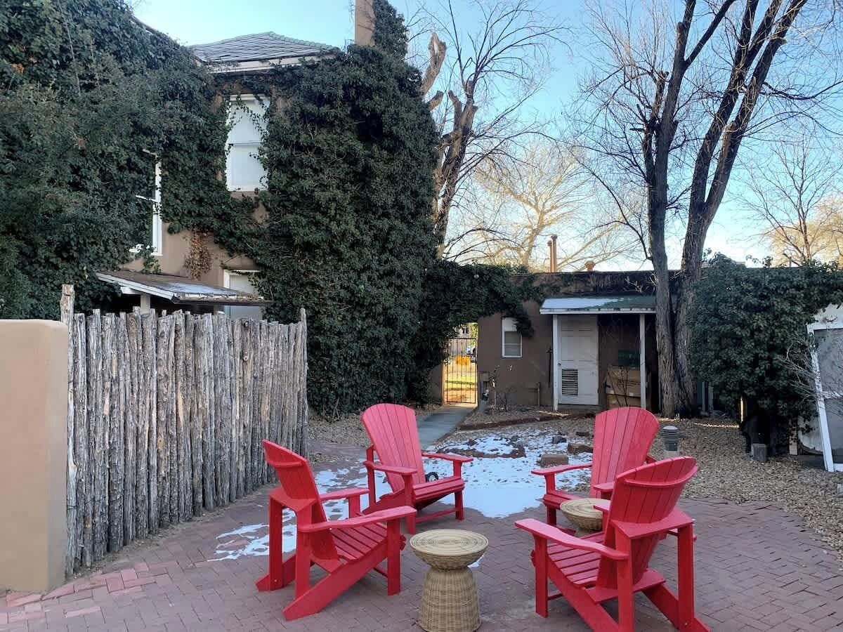 Un jardín trasero con cerco de madera, patio de ladrillo y sillas Adirondack rojas.