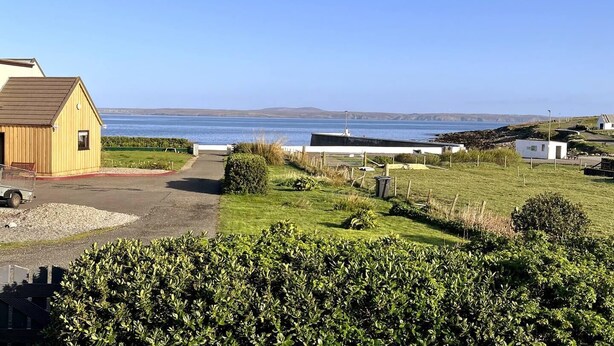 Una propiedad costera con un camino de entrada pavimentado que lleva a un edificio, un área verde con arbustos y vistas al mar.
