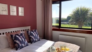 Un dormitorio con cama, almohadas, una bandeja de desayuno y una ventana con vista a follaje.
