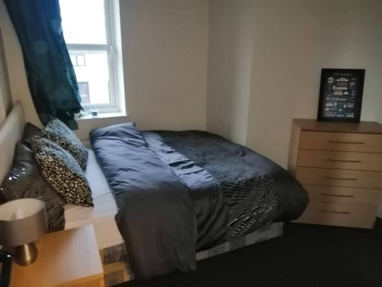 A bedroom with a bed, a bedside table, a lamp, a dresser, and a window.