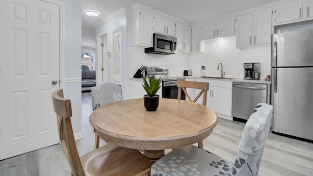 A modern kitchen with white cabinetry, stainless steel appliances, and a round wooden table with chairs. - Newly Remodeled Townhome(RD) (North Charleston)