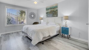 A bedroom with a bed, a ceiling fan, a nightstand with a lamp, a wall clock, and a painting. - Newly Remodeled Townhome(RD) (North Charleston)