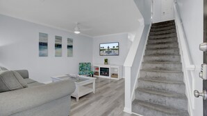 A modern living room with a grey sofa, a white coffee table, and a fireplace. There is a staircase leading to another level. - Newly Remodeled Townhome(RD) (North Charleston)