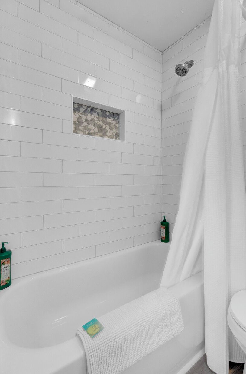 Ein Badezimmer mit weißen Fliesen, einer Dusche und einer Badewanne.