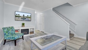 A modern living room with a fireplace, a television mounted on the wall, a staircase, and a glass coffee table. - Newly Remodeled Townhome(RD) (North Charleston)