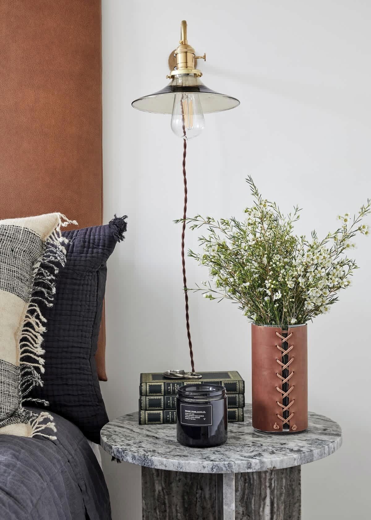 Une table de chevet avec une lampe, une plante en pot et un livre.