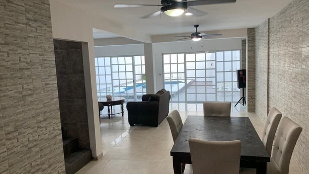 A spacious dining area with a high ceiling fan, a large window offering a view of the outside, and a modern interior design. - Magnífica casa con piscina privada a 10 min del mar (Cancún)
