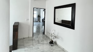 A hallway with white walls, a marble floor, a potted plant, and a framed mirror. - Magnífica casa con piscina privada a 10 min del mar (Cancún)