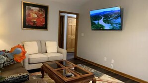 Ein Wohnzimmer mit einer Couch, einem Couchtisch, einem Gemälde und einem Fernseher, der eine Landschaft zeigt.