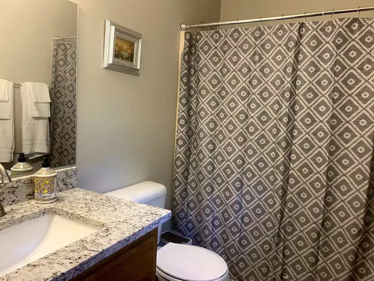 A bathroom with a granite countertop, a toilet, and a shower curtain with a diamond pattern.