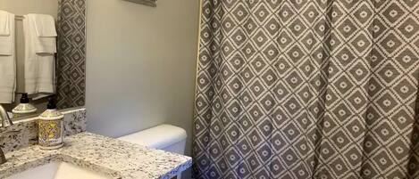 A bathroom with a granite countertop, a toilet, and a shower curtain with a diamond pattern.