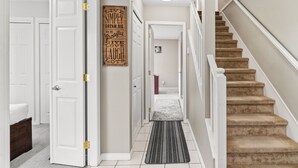 A hallway with white doors, a wooden sign with motivational phrases, a carpeted staircase, and a white bench. - Beautiful Home in Langley with Huge Patio (Langley)