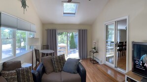 Ein Wohnzimmer mit einer Couch, einem Fernseher und Blick ins Freie.