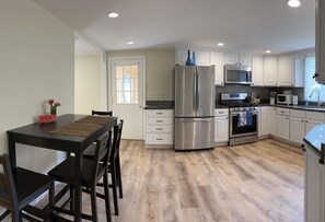 A modern kitchen with white cabinets, stainless steel appliances, and a wooden floor.