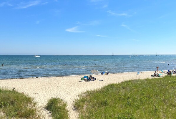 A beach with a sandy shore, a few boats in the water, and people relaxing under umbrellas.