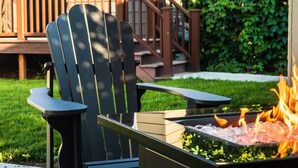 Una silla Adirondack negra con apoyabrazos y un hogar para fuego de metal con llamas.