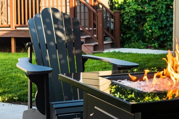 A black Adirondack chair with armrests and a metal fire pit with flames.