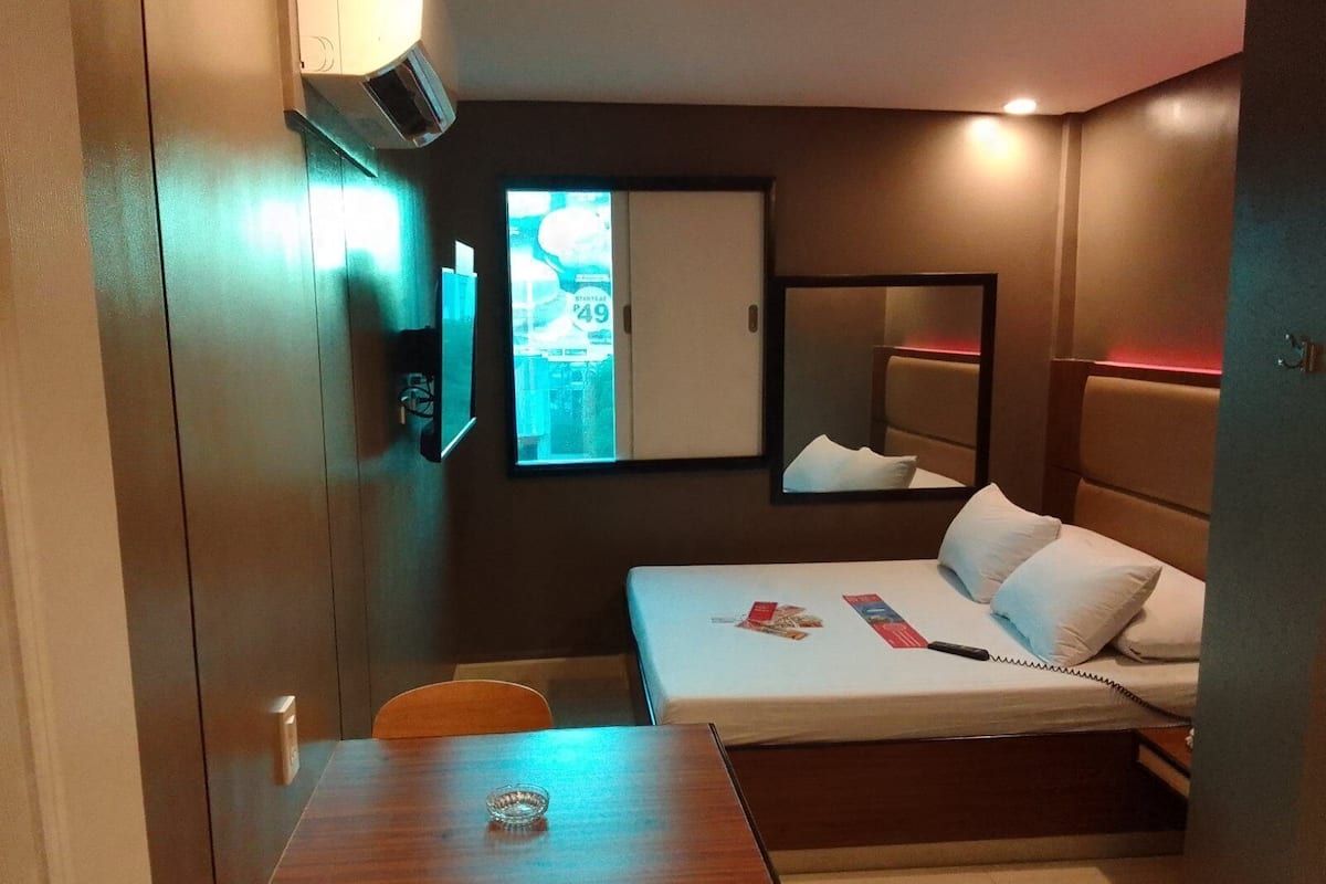 A hotel room with a bed, bedside table, chair, and a window with a view.