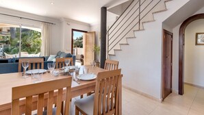 A dining area with a wooden table set for four, a staircase with a modern design, and a view of the outdoors through large windows.